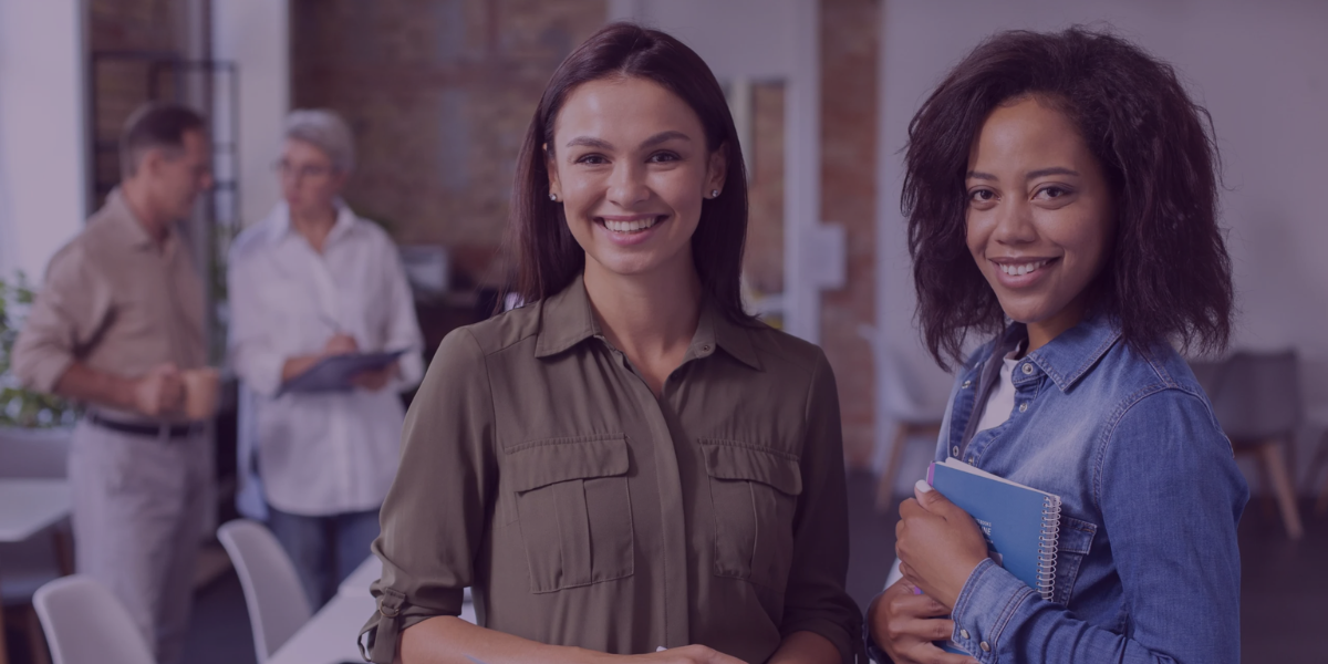 Duas mulheres sorrindo em um ambiente de trabalho, representando áreas de Recursos Humanos e Departamento Pessoal.